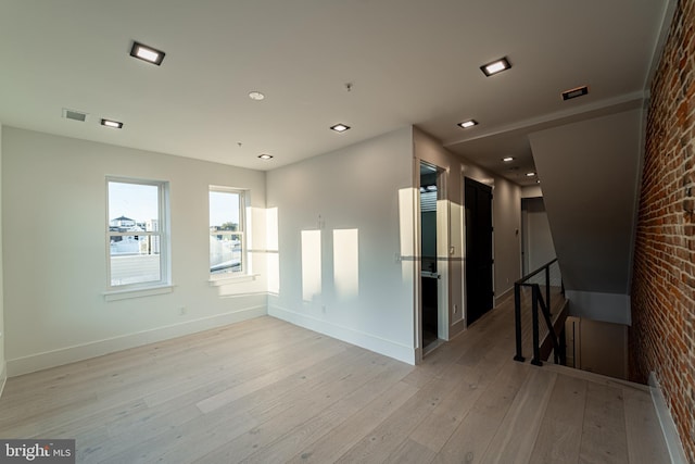 spare room with light wood finished floors, brick wall, visible vents, and baseboards