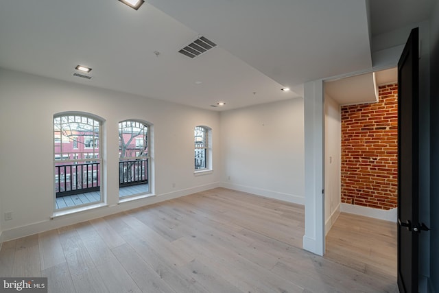 spare room featuring light wood finished floors, visible vents, baseboards, brick wall, and recessed lighting