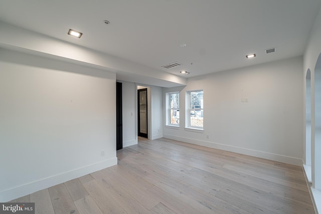 empty room featuring light wood-style floors, baseboards, visible vents, and arched walkways