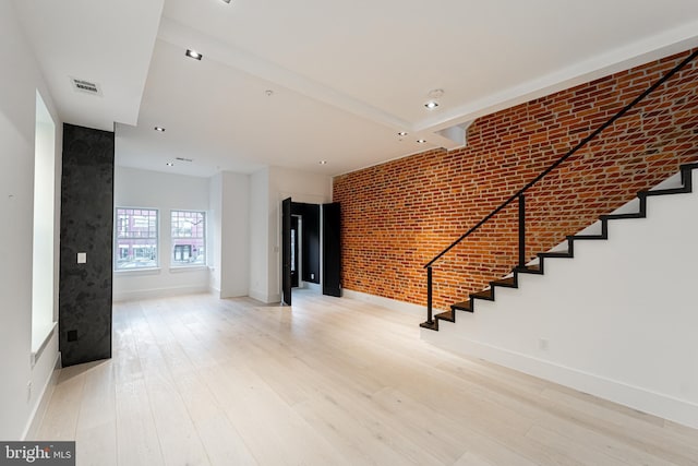 interior space with light wood-type flooring, baseboards, stairway, and brick wall