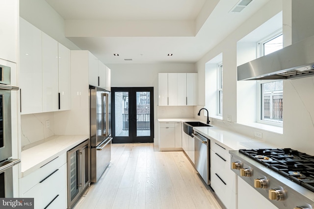 kitchen with appliances with stainless steel finishes, modern cabinets, beverage cooler, and extractor fan