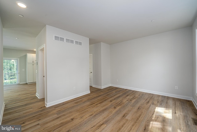 spare room with wood finished floors, visible vents, and baseboards