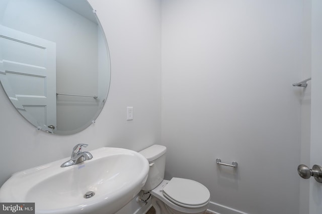 half bath with baseboards, a sink, and toilet