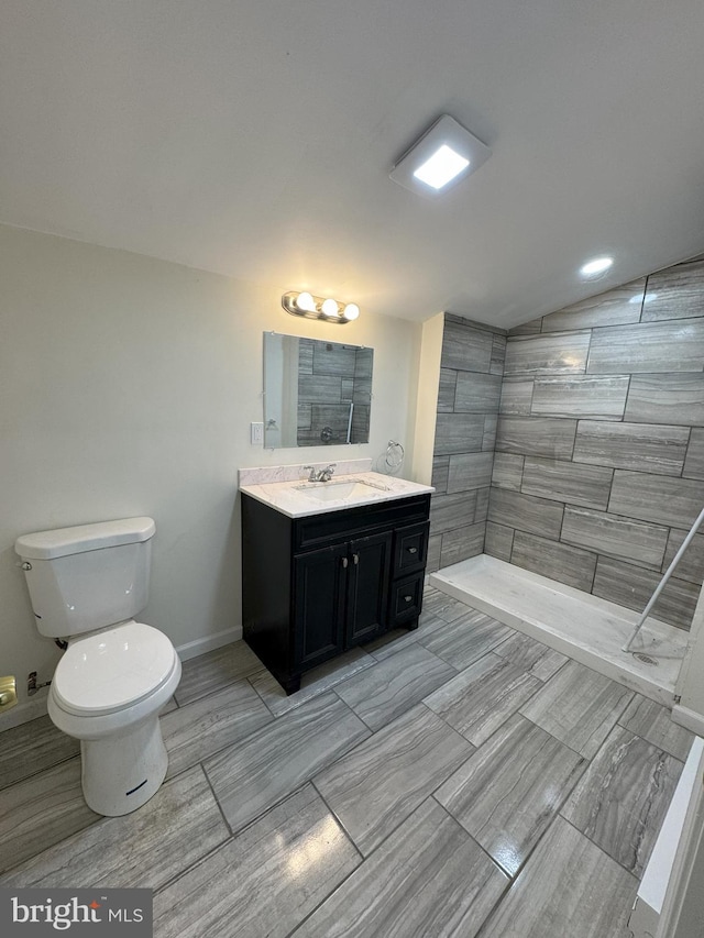 bathroom featuring toilet, vanity, baseboards, vaulted ceiling, and a tile shower