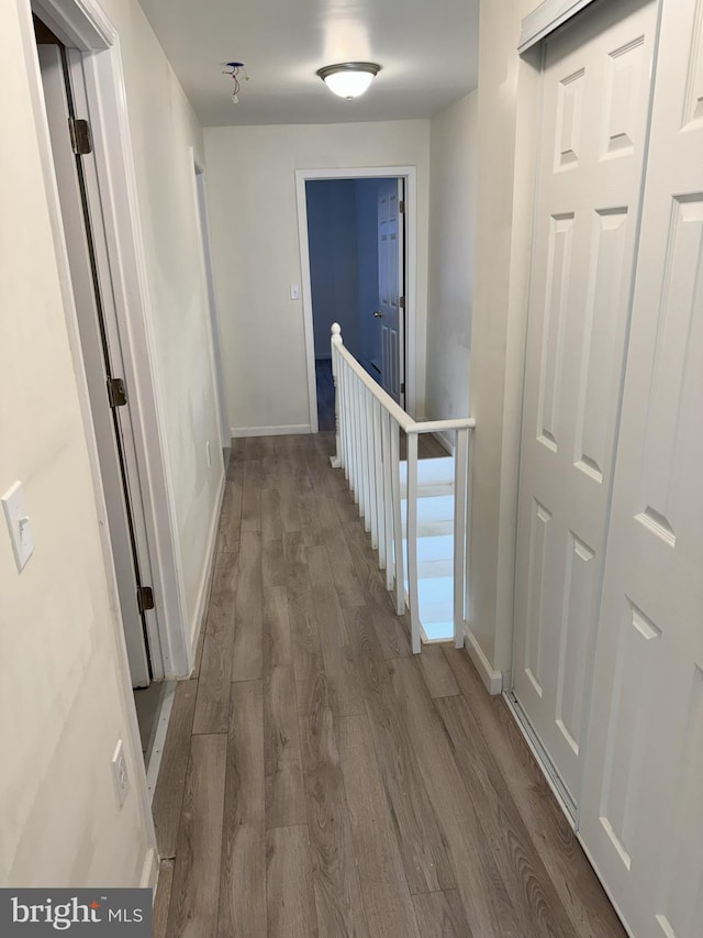 corridor with baseboards, an upstairs landing, and wood finished floors