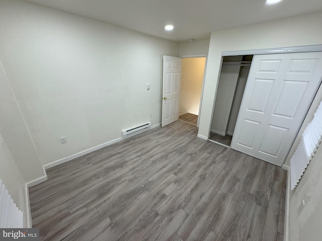 unfurnished bedroom featuring a baseboard radiator, a closet, baseboards, and wood finished floors