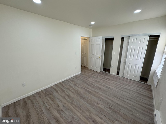 unfurnished bedroom with recessed lighting, baseboards, multiple closets, and wood finished floors