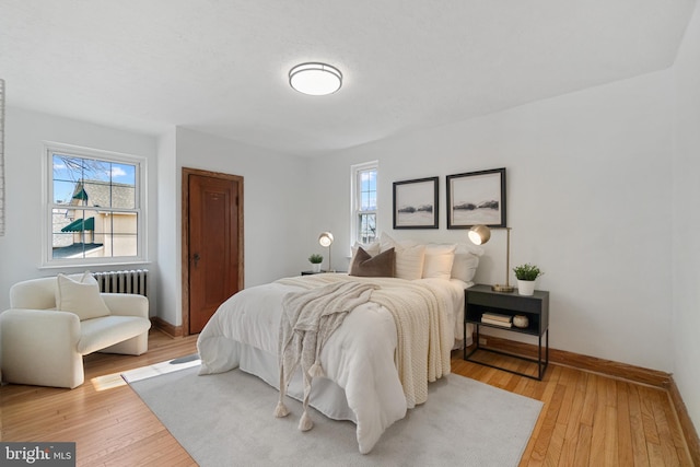 bedroom featuring light wood-type flooring, radiator heating unit, and baseboards