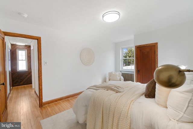 bedroom with baseboards, multiple windows, light wood-style flooring, and radiator heating unit