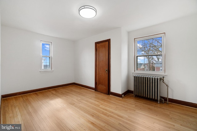 unfurnished bedroom featuring light wood-style floors, baseboards, and radiator heating unit