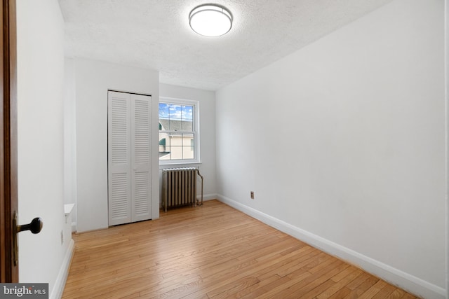 unfurnished bedroom with baseboards, radiator, light wood-style flooring, a textured ceiling, and a closet