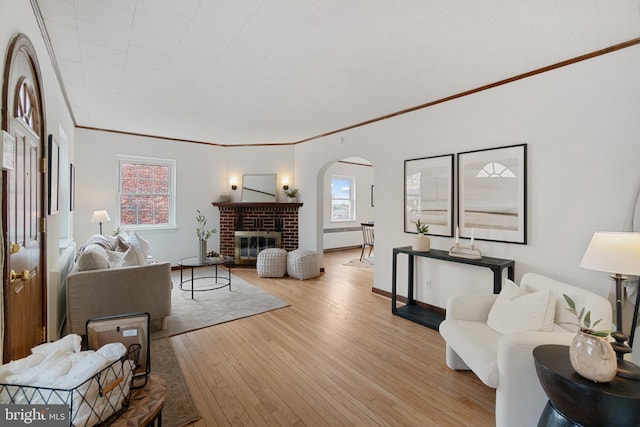 living area featuring a brick fireplace, ornamental molding, arched walkways, and wood finished floors