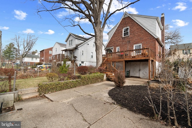 rear view of house with concrete driveway, a chimney, a residential view, a wooden deck, and brick siding