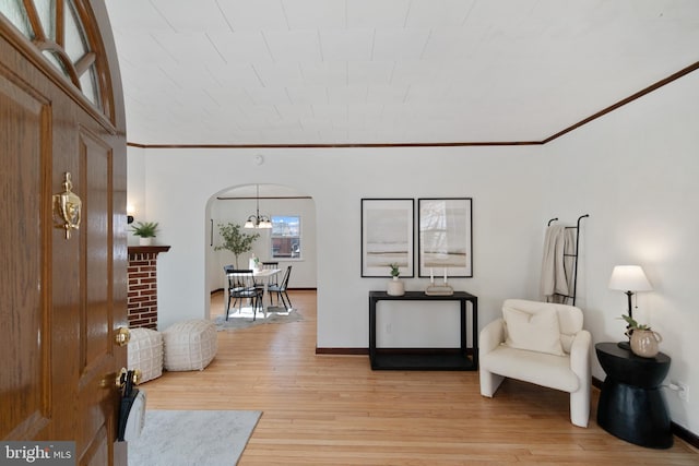 entryway featuring light wood-style floors, arched walkways, crown molding, and baseboards