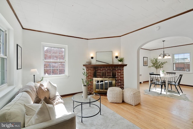 living area with light wood-style floors, arched walkways, a fireplace, and baseboards