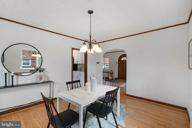 dining room with light wood-style flooring, arched walkways, baseboards, and ornamental molding