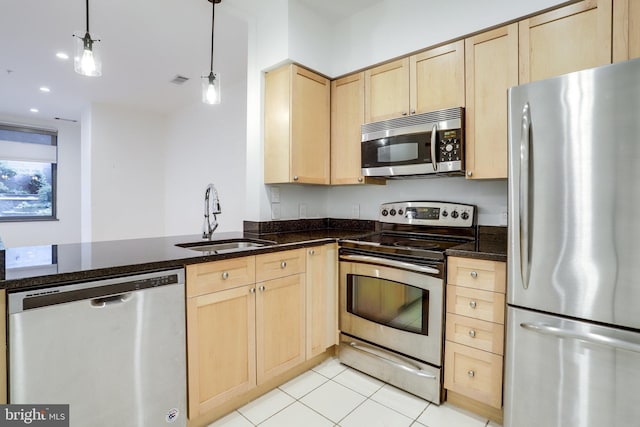 kitchen with light brown cabinets, light tile patterned floors, dark stone countertops, stainless steel appliances, and a sink