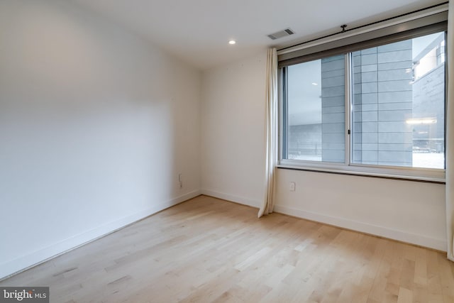 spare room featuring light wood-style floors, baseboards, visible vents, and a wealth of natural light