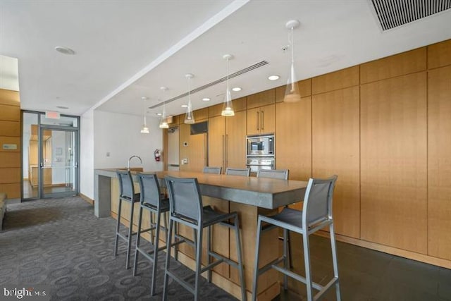 kitchen featuring visible vents, a breakfast bar, stainless steel appliances, pendant lighting, and brown cabinets