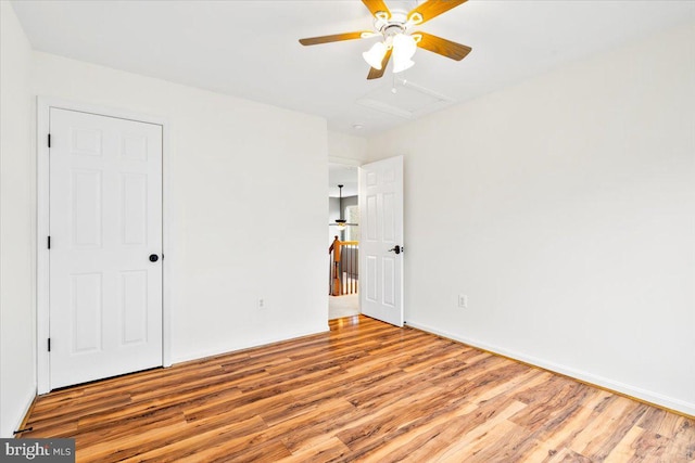 unfurnished bedroom with attic access, ceiling fan, and wood finished floors