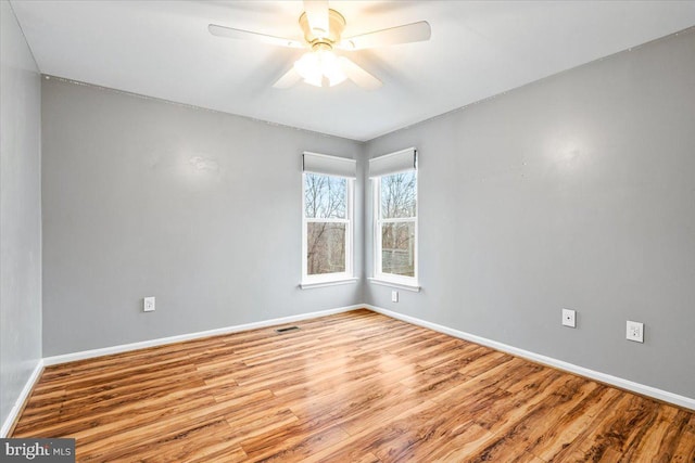 empty room with a ceiling fan, visible vents, baseboards, and wood finished floors