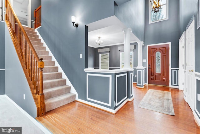 foyer entrance with a notable chandelier, crown molding, wood finished floors, and ornate columns