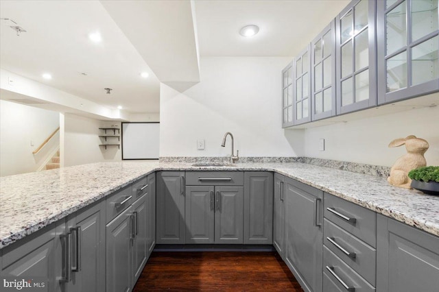 kitchen featuring dark wood-style floors, gray cabinets, a sink, and light stone counters