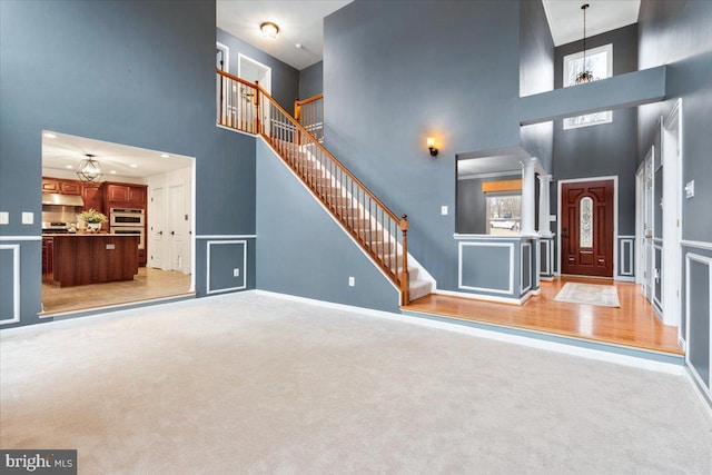 entryway featuring light colored carpet, a notable chandelier, a towering ceiling, and stairs