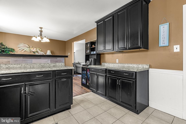 kitchen featuring an inviting chandelier, open shelves, dark cabinets, and wainscoting