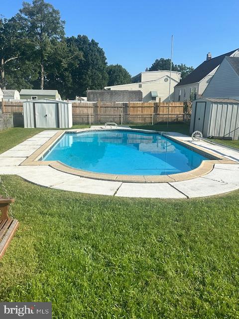 view of swimming pool featuring an outbuilding, a fenced backyard, a lawn, and a storage unit