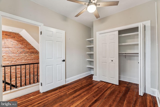 unfurnished bedroom featuring ceiling fan, brick wall, wood finished floors, baseboards, and a closet