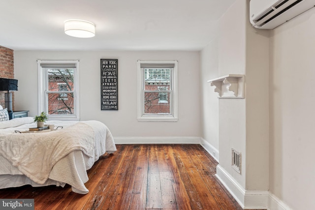 bedroom with a wall unit AC, hardwood / wood-style flooring, visible vents, and baseboards