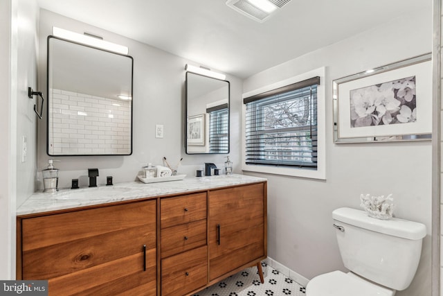 full bathroom with toilet, a sink, visible vents, baseboards, and double vanity