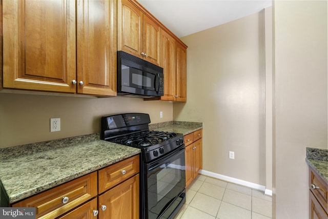 kitchen with brown cabinetry, light tile patterned flooring, black appliances, light stone countertops, and baseboards