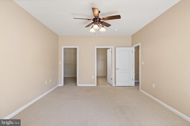 unfurnished bedroom with baseboards, a spacious closet, ceiling fan, and light colored carpet