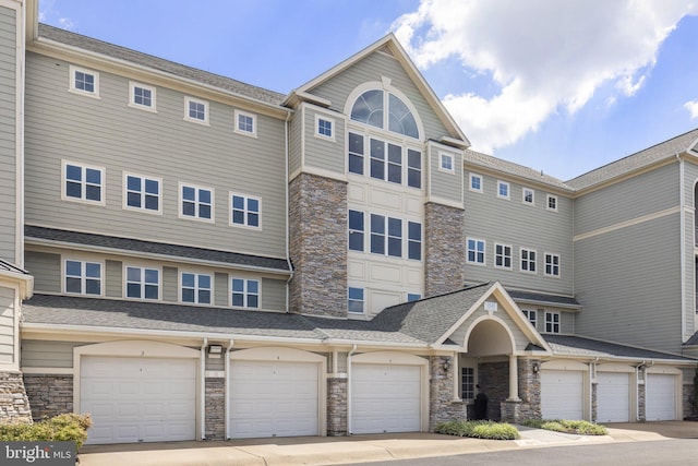 townhome / multi-family property with a shingled roof and stone siding