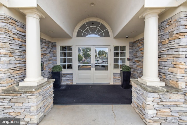 property entrance with stone siding, stucco siding, a porch, and french doors