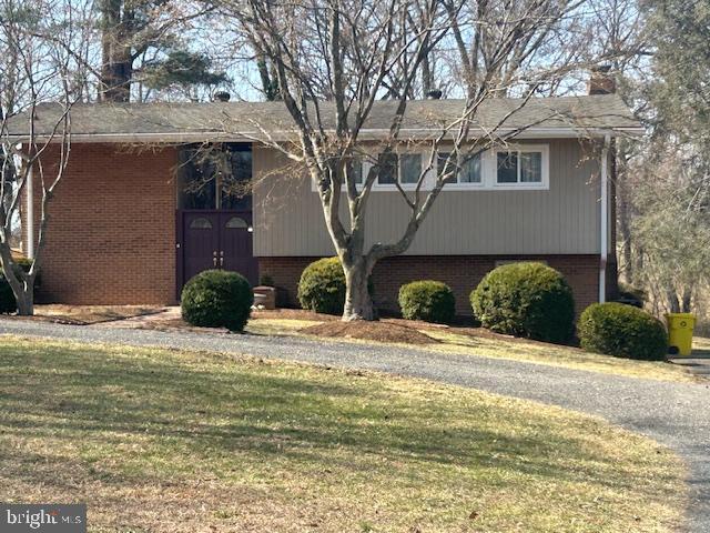 view of front of house with gravel driveway, a front yard, a chimney, and brick siding