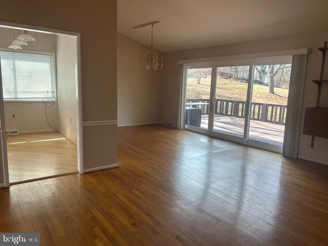 unfurnished dining area with wood finished floors, visible vents, baseboards, vaulted ceiling, and an inviting chandelier