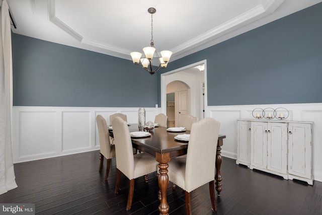 dining space with arched walkways, dark wood-type flooring, a notable chandelier, and wainscoting