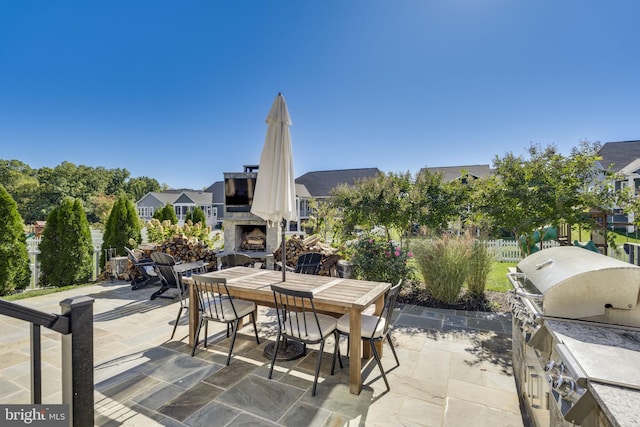 view of patio with an outdoor stone fireplace, fence, outdoor dining area, and area for grilling