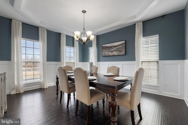 dining space with crown molding, dark wood-style flooring, wainscoting, and a notable chandelier