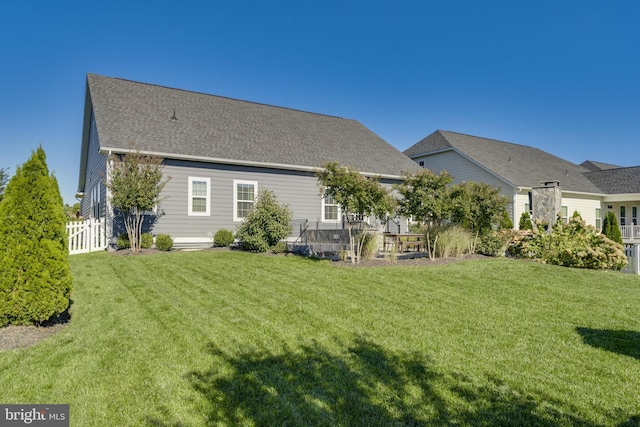 rear view of house with a yard, roof with shingles, and fence