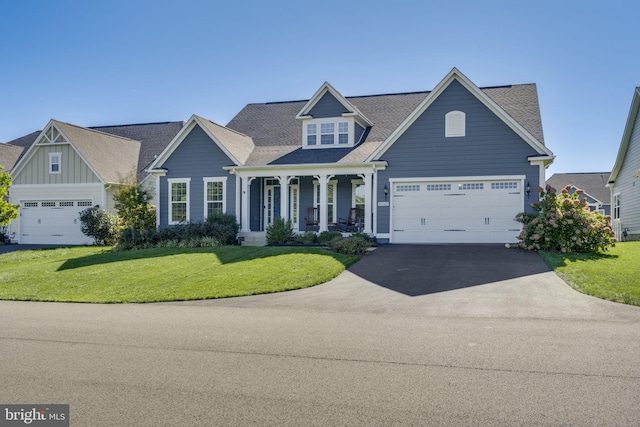 view of front of property featuring aphalt driveway, a garage, covered porch, roof with shingles, and a front lawn