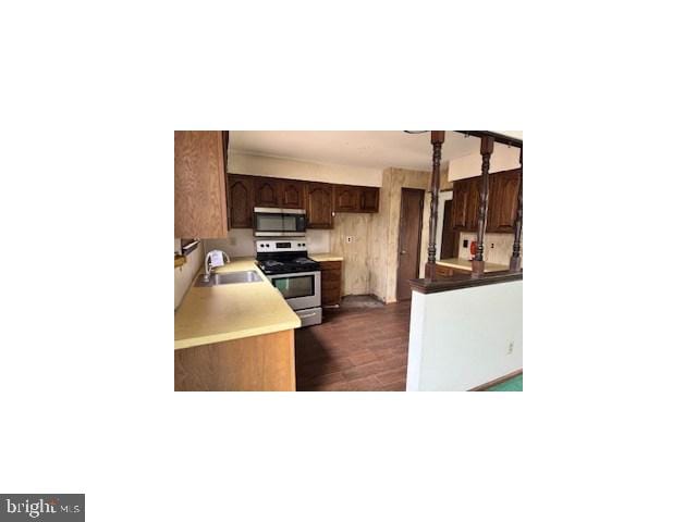 kitchen with dark wood-style floors, appliances with stainless steel finishes, dark brown cabinets, and a sink