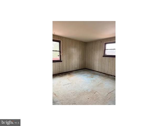 unfurnished room with unfinished concrete flooring and wood walls