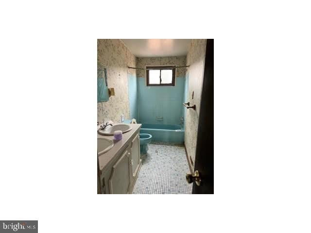 full bathroom with double vanity, wallpapered walls, bathing tub / shower combination, toilet, and a sink