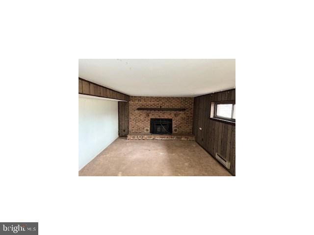 unfurnished living room featuring a brick fireplace, wooden walls, baseboard heating, and concrete flooring