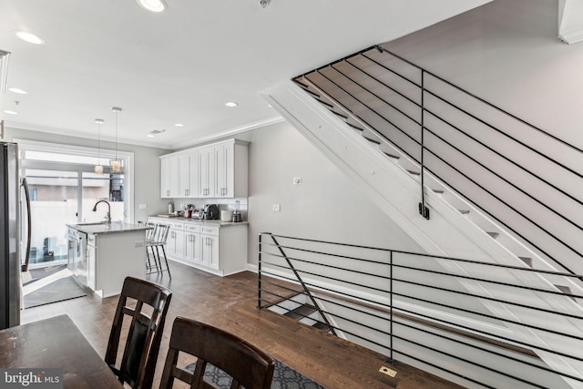 kitchen featuring recessed lighting, ornamental molding, freestanding refrigerator, a kitchen island with sink, and a sink