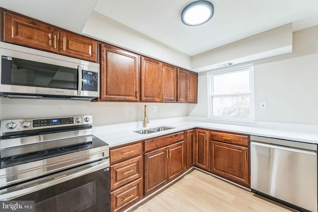 kitchen featuring light wood-style flooring, stainless steel appliances, a sink, light countertops, and brown cabinetry